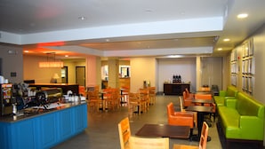 A spacious indoor dining area with multiple wooden tables and chairs, a blue counter with a coffee machine, and a green sofa.