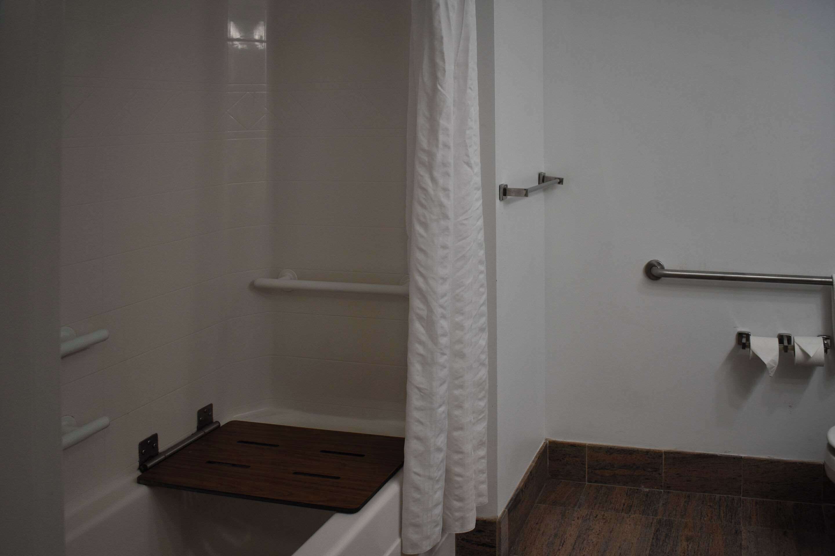 Un baño con ducha, un banco de madera, un perchero y un inodoro.