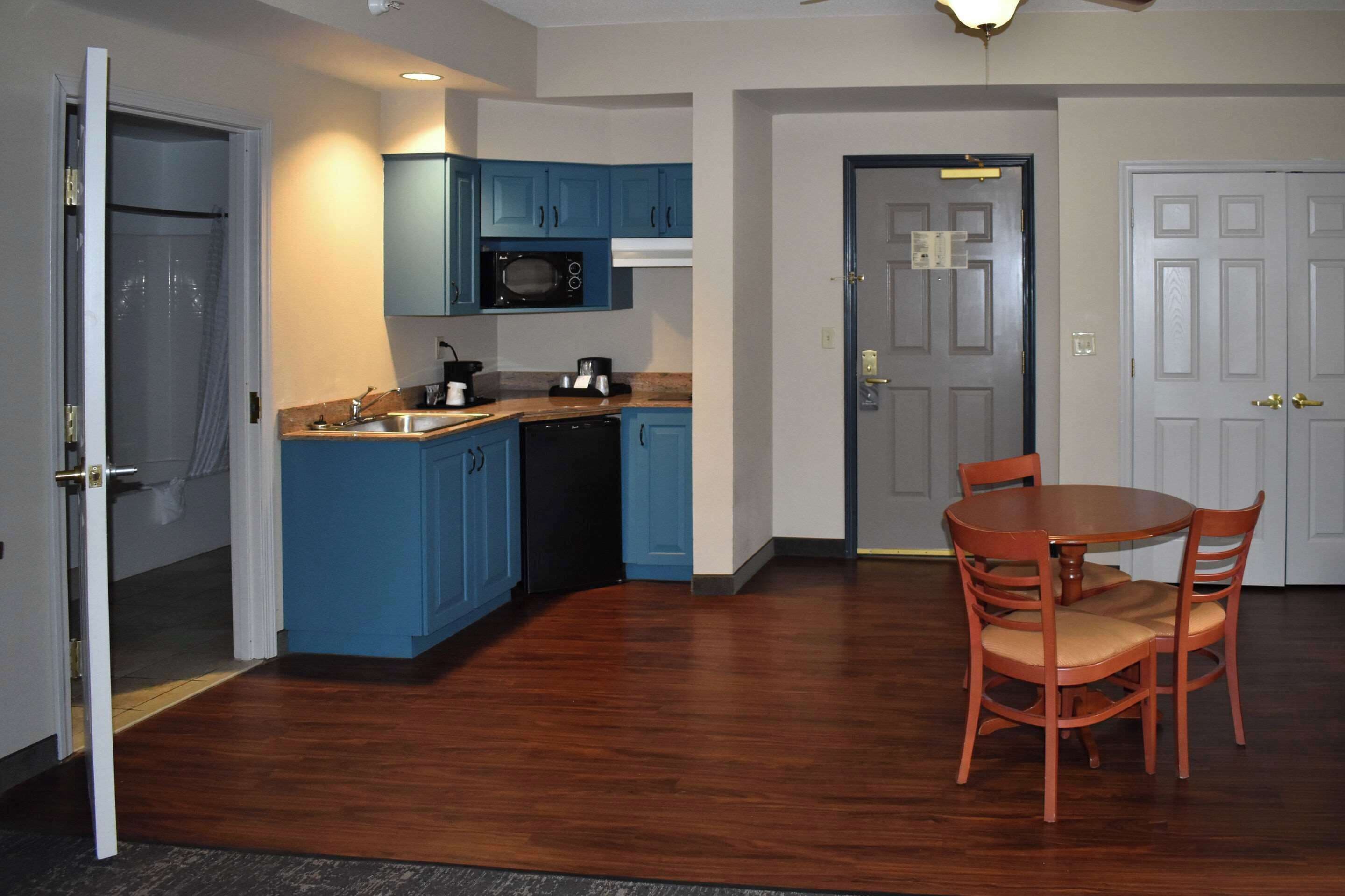 A compact kitchen with blue cabinets, a microwave, and a dishwasher. There is a dining table with chairs and a door leading to another room.