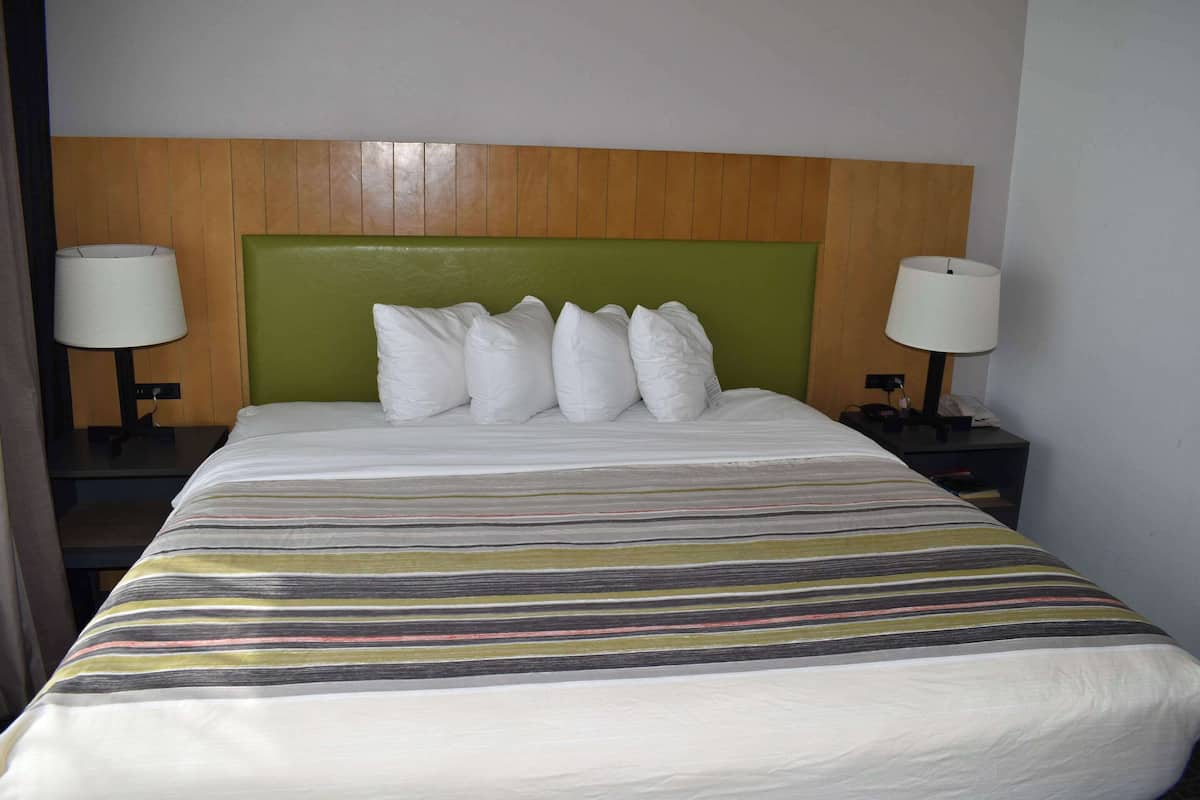 A hotel room with a bed, a green headboard, white pillows, and two bedside lamps.