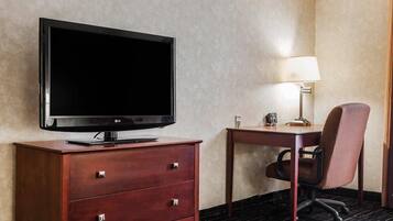 Habitación de hotel con televisión de pantalla plana sobre un aparador de madera, un escritorio con lámpara y una silla.