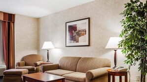 Quarto de hotel com sofá, poltrona e uma mesinha. Há uma luminária em cada lado do sofá e uma planta em vaso à direita.