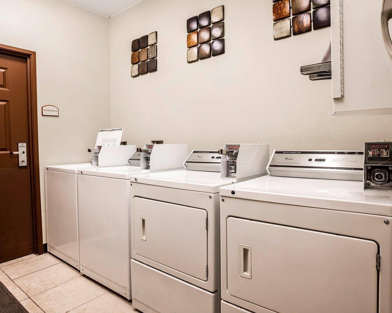 Un espace buanderie comprenant trois machines à laver et trois sèche-linge superposés, une balance fixée au mur et une porte portant l’inscription « ATELIER ».
