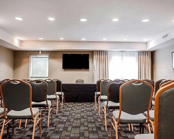 Un salón de conferencias con filas de sillas, una pantalla para proyector y un amplio ventanal con cortinas.