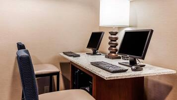 Una habitación de hotel con un escritorio, dos monitores, un teclado, un ratón, una lámpara y una silla.