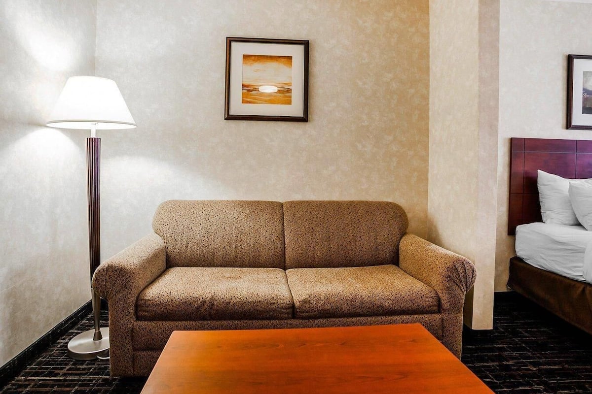 A hotel room with a sofa, a small table, a lamp, and a bed with a headboard.