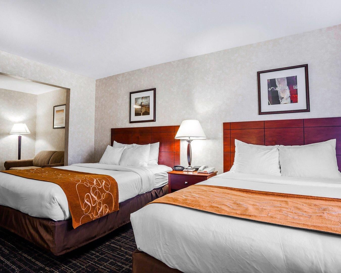 A hotel room with two beds, a nightstand with a lamp, and framed artwork on the walls.
