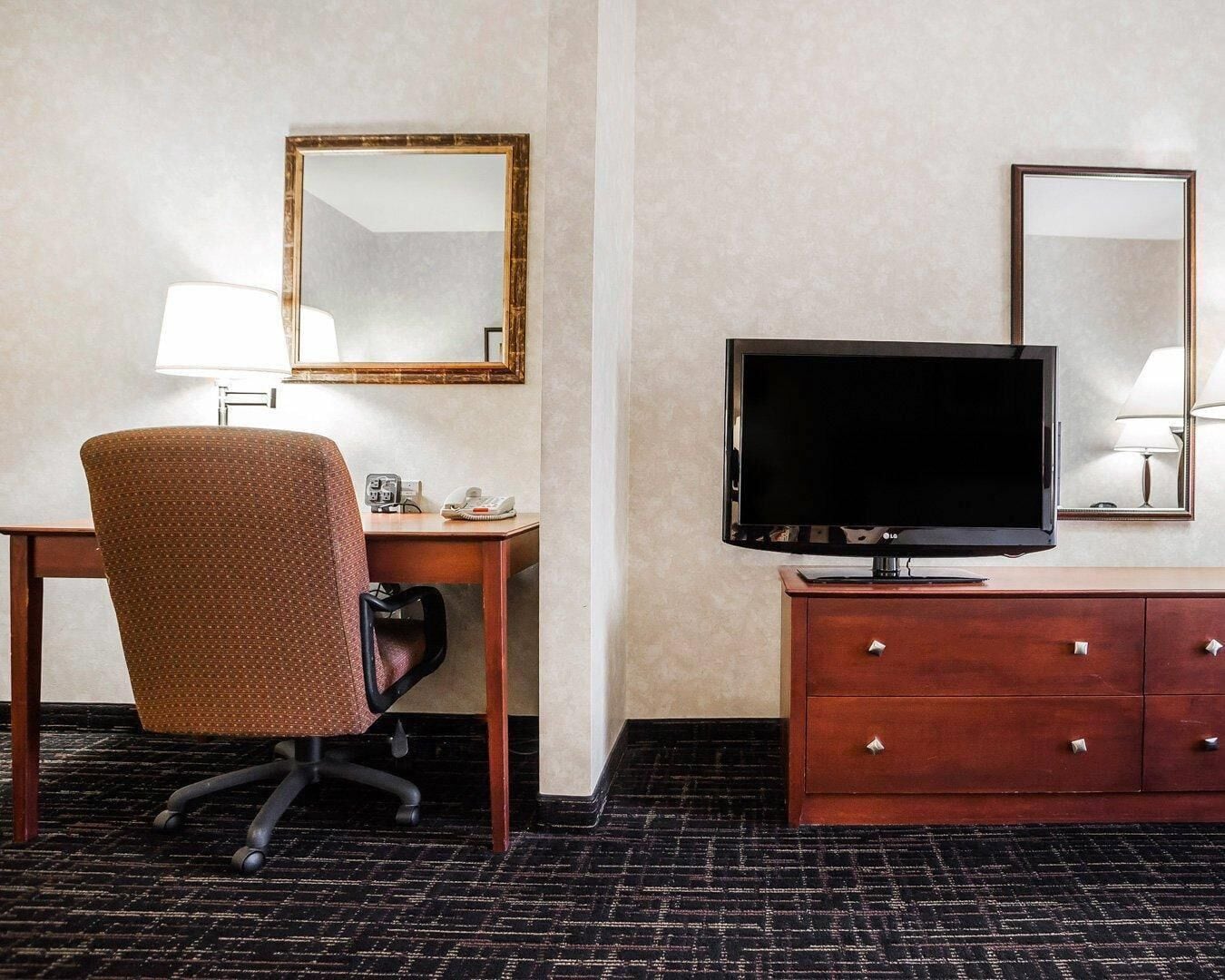 Hotellihuone, jossa on työpöytä, tuoli, televisio ja peili.