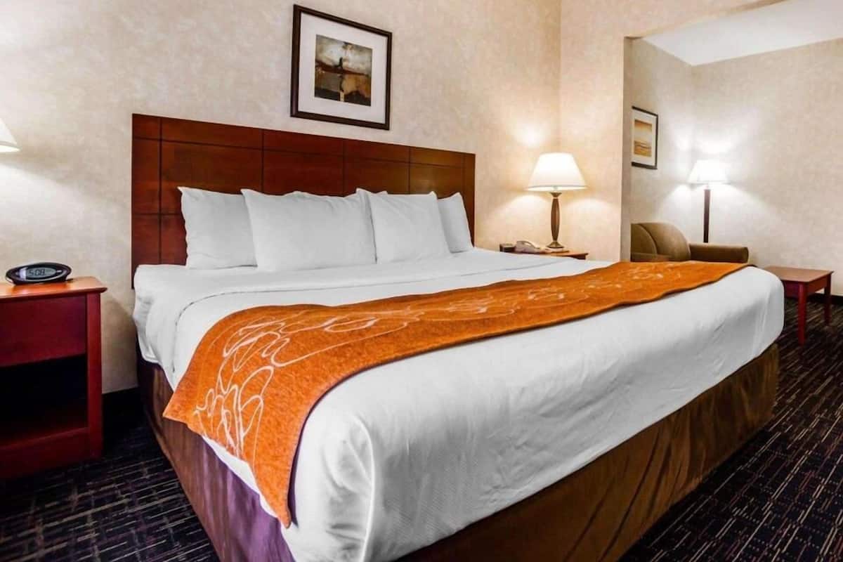 A hotel room with a large bed, two bedside tables, a nightstand, a chair, a framed picture on the wall, and a lamp on each bedside table.