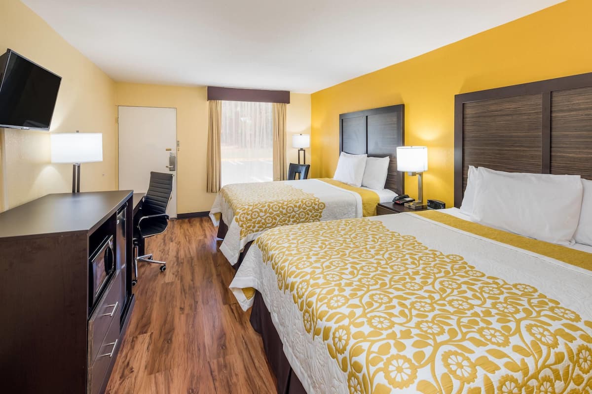 A hotel room with two beds, a desk, a chair, a television, and a door.