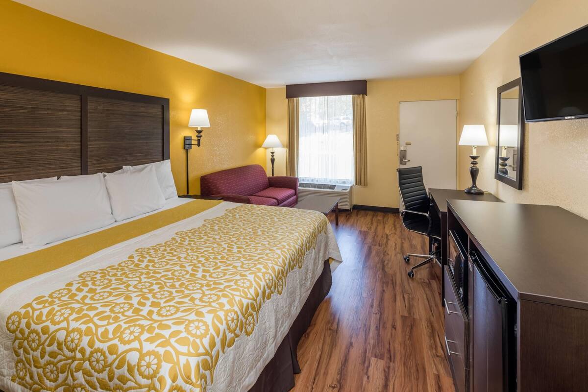 A hotel room with a bed, a desk, a chair, a TV, and a window.