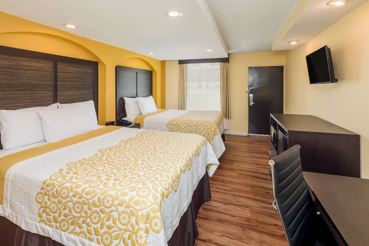 A hotel room with two beds, a desk, a TV, and a window with curtains.