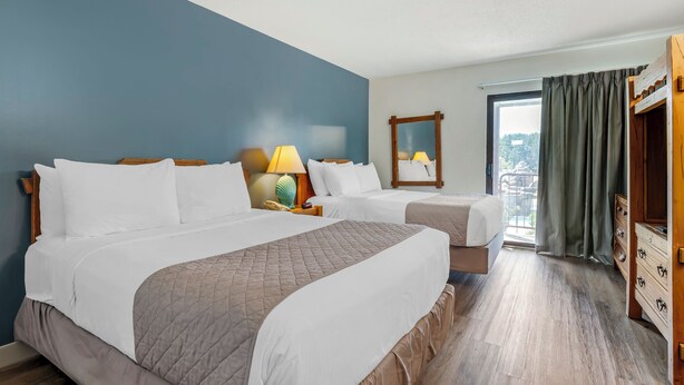 A hotel room with two beds, a wooden dresser, a nightstand with a lamp, and a large window with curtains. - Polynesian Hotel & Suites Wisconsin Dells/Lake Delton (Wisconsin Dells)