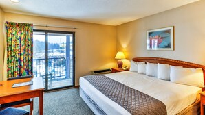 Ett hotellrum med en stor säng, ett skrivbord, en stol, ett fönster med färgglada gardiner och utsikt över omgivningarna.