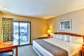 Une chambre d’hôtel avec un grand lit, un bureau, une chaise, une fenêtre avec des rideaux colorés et une vue sur l’extérieur.