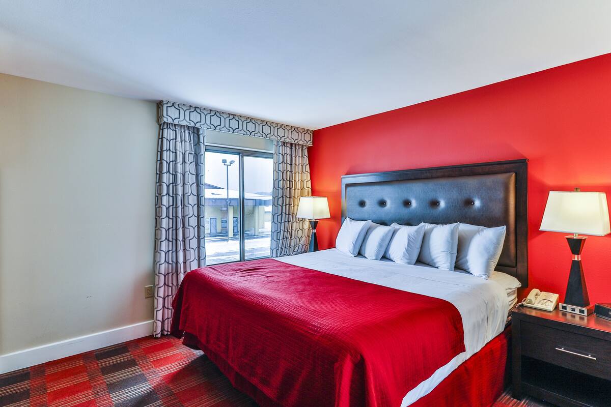 Habitación de hotel con una cama grande, paredes rojas y vistas al exterior.