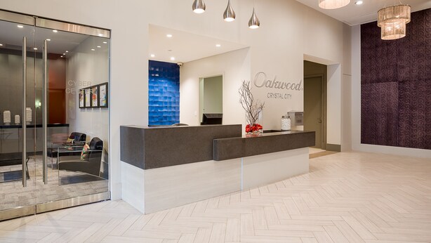 A modern reception area with a glass wall, a reception desk, and a wall-mounted sign reading "Oakwood Crystal City." - Oakwood Crystal City (Arlington)