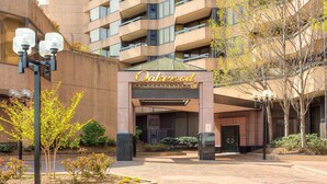 A hotel entrance with a sign reading "Oakwood," surrounded by a landscaped area with trees and shrubs. - Oakwood Crystal City (Arlington)