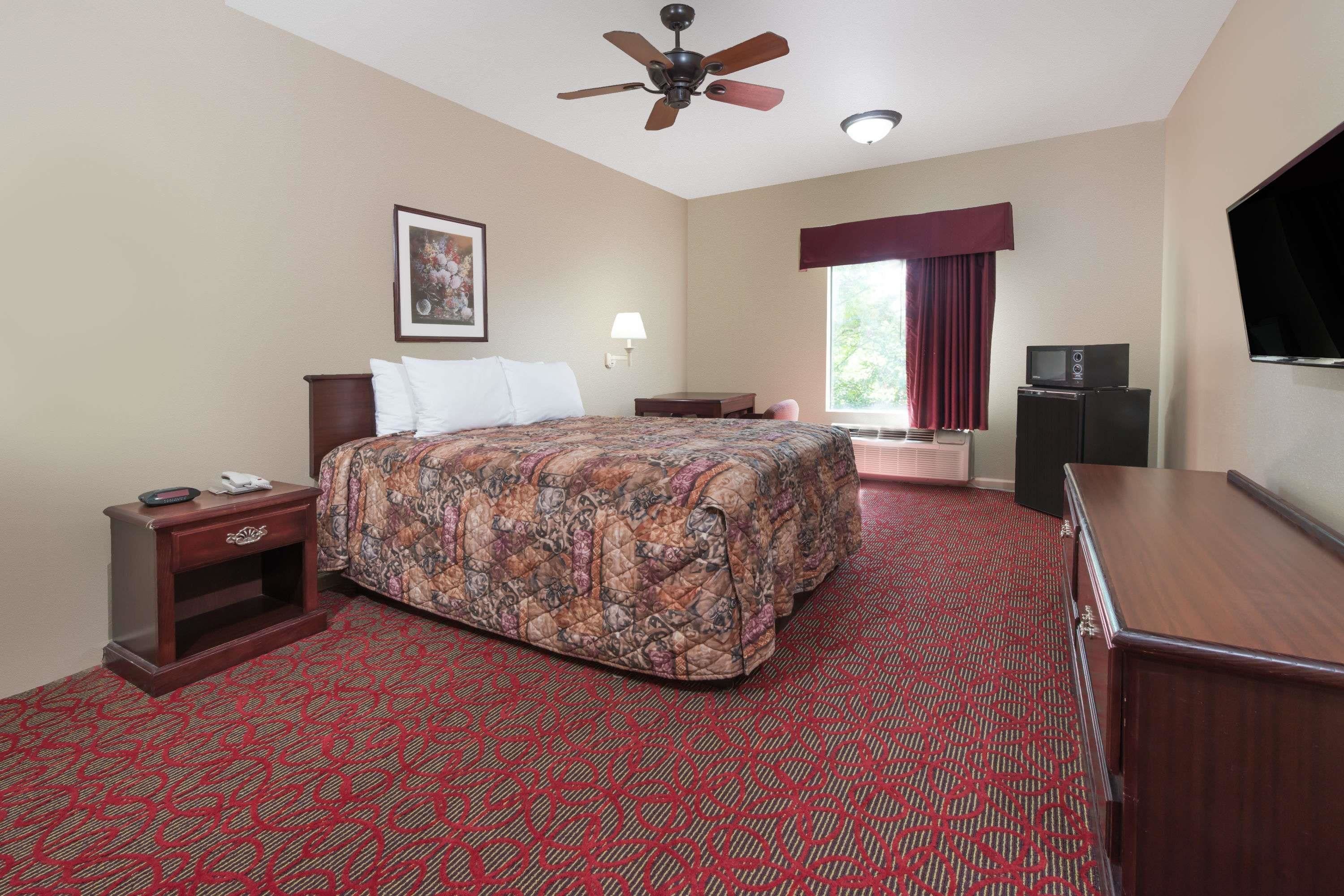 Habitación de hotel con una cama grande, ventilador de techo, televisión, escritorio y ventana con cortinas.