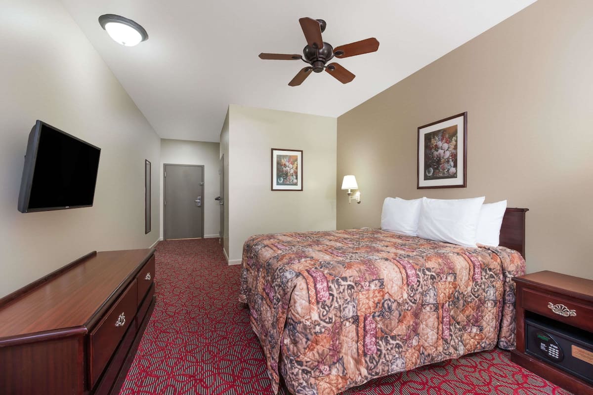 A hotel room with a bed, a TV, a ceiling fan, a desk, and a safe.