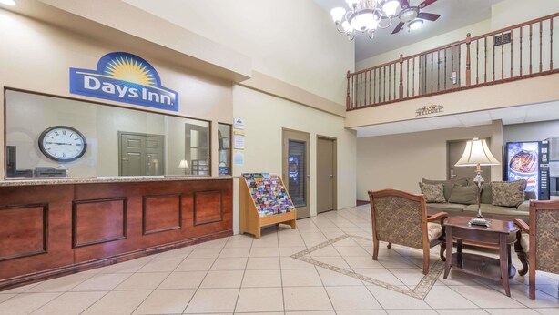 A Days Inn lobby with a reception desk, a clock, a small coffee table, and a sofa. - Days Inn by Wyndham St Peters/St Charles (St. Peters)