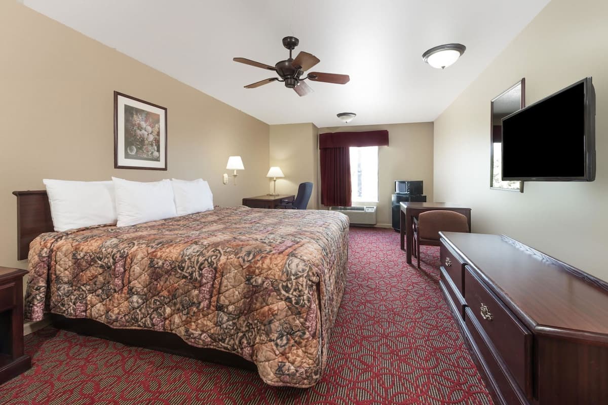 A hotel room with a bed, a desk, a television, a ceiling fan, and a window with curtains.