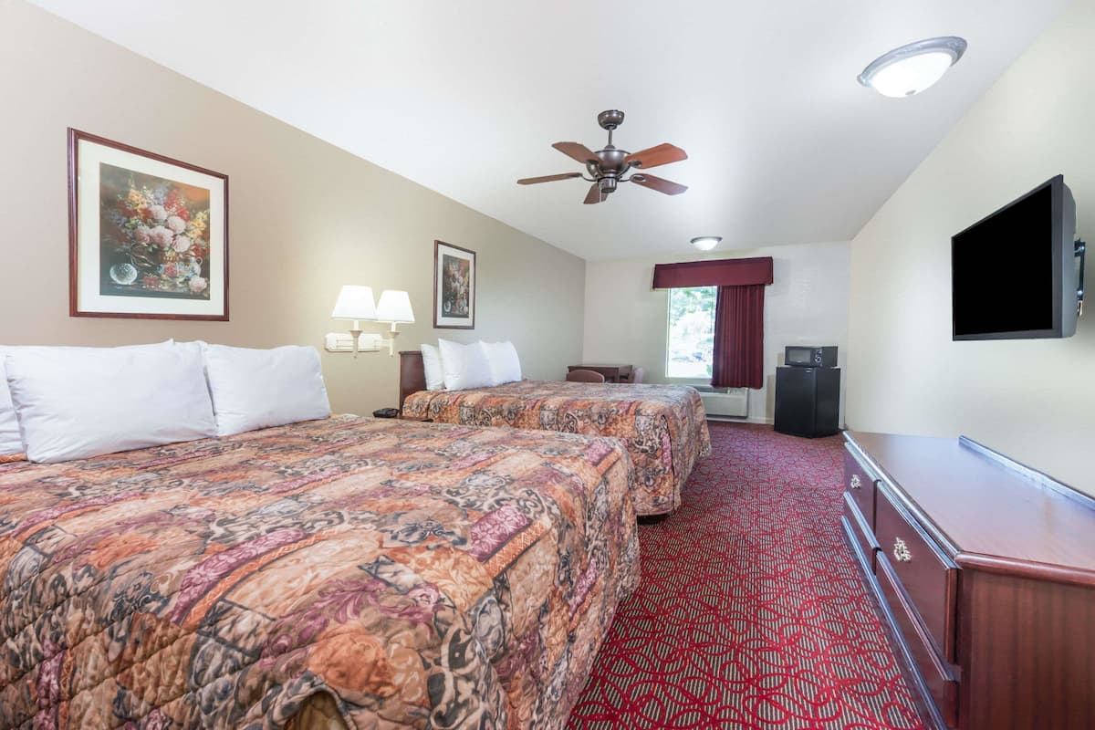 A hotel room with two beds, a ceiling fan, a flat-screen TV, a desk, and a red carpeted floor.