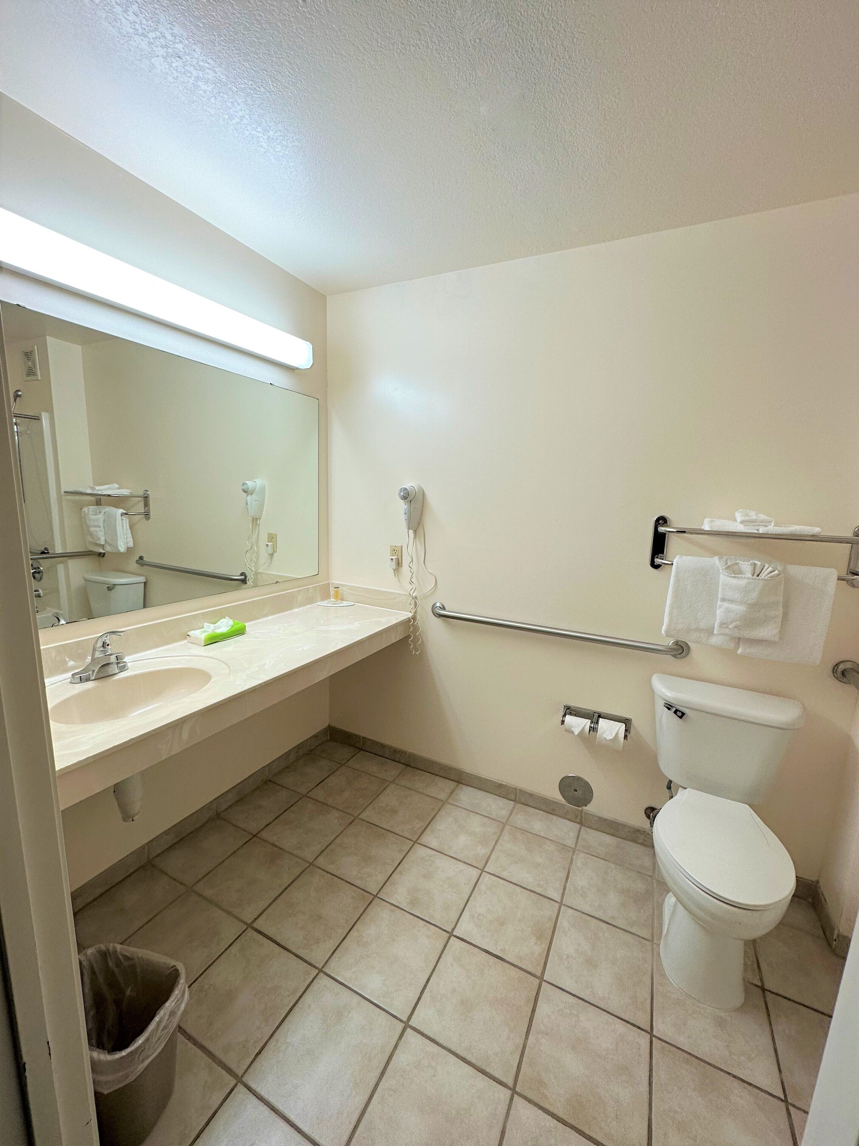 Une salle de bain équipée d’un lavabo, d’un miroir, d’un porte-serviettes, de toilettes et d’une poubelle.
