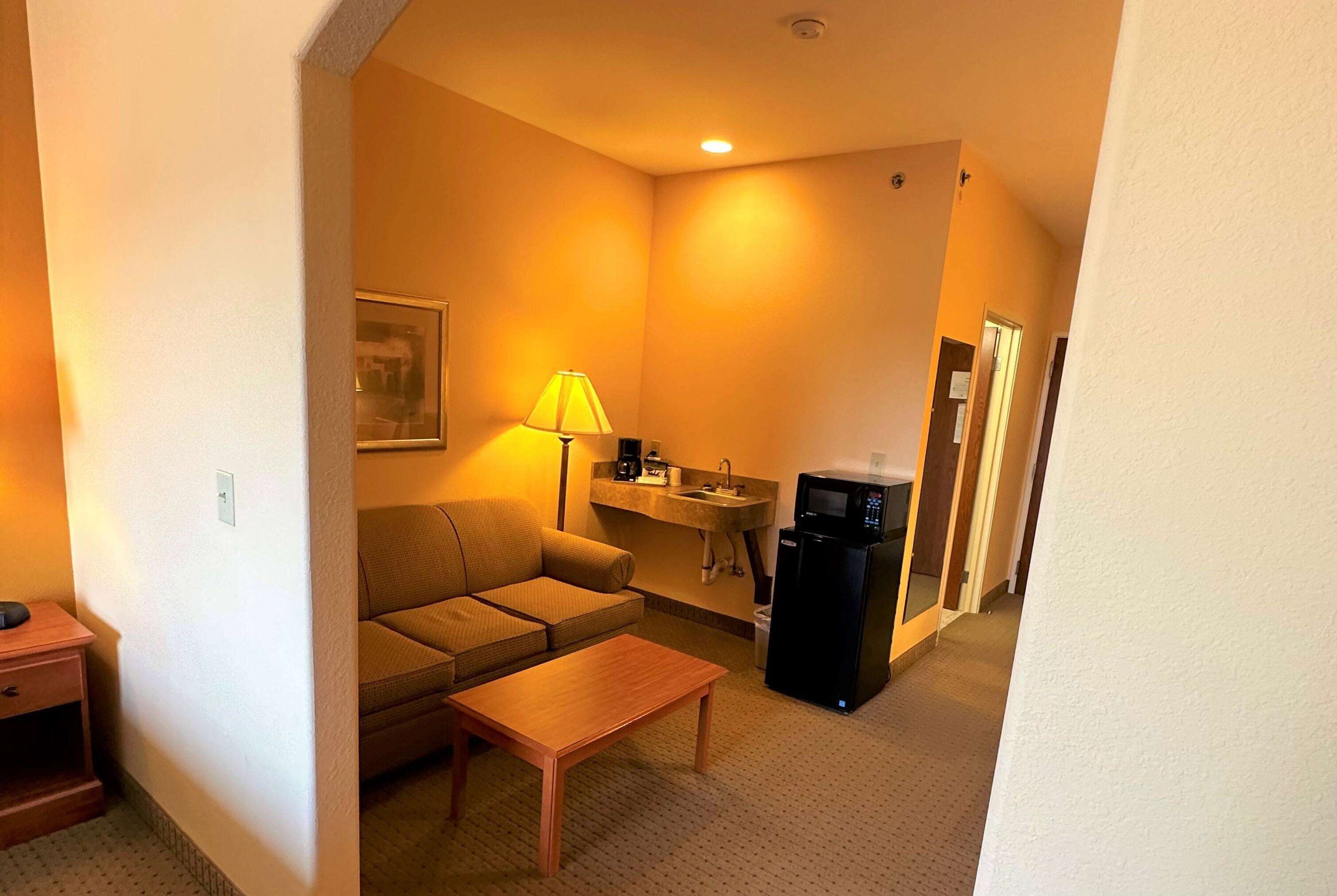 A compact living space with a sofa, a coffee table, a lamp, a microwave, and a small kitchenette.