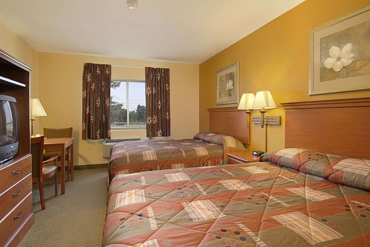 Ein Hotelzimmer mit zwei Betten, einem Schreibtisch mit Stuhl, einem Fernseher und einem Fenster mit Vorhängen.