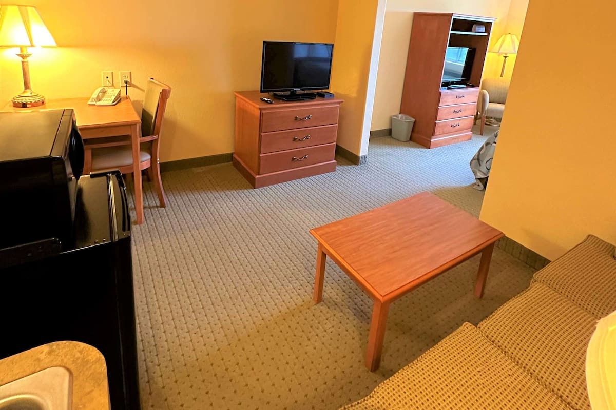 Ein Hotelzimmer mit einem Holztisch, einem Fernseher auf einer Kommode, einem Sofa und einem kleinen Tisch.