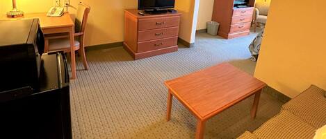 Una habitación de hotel con un escritorio de madera, un televisor en una cómoda, un sofá y una mesita.