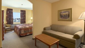 A hotel room with a bed, a sofa, a chair, a table, and a window with curtains. - Super 8 by Wyndham Topeka at Forbes Landing (Topeka)