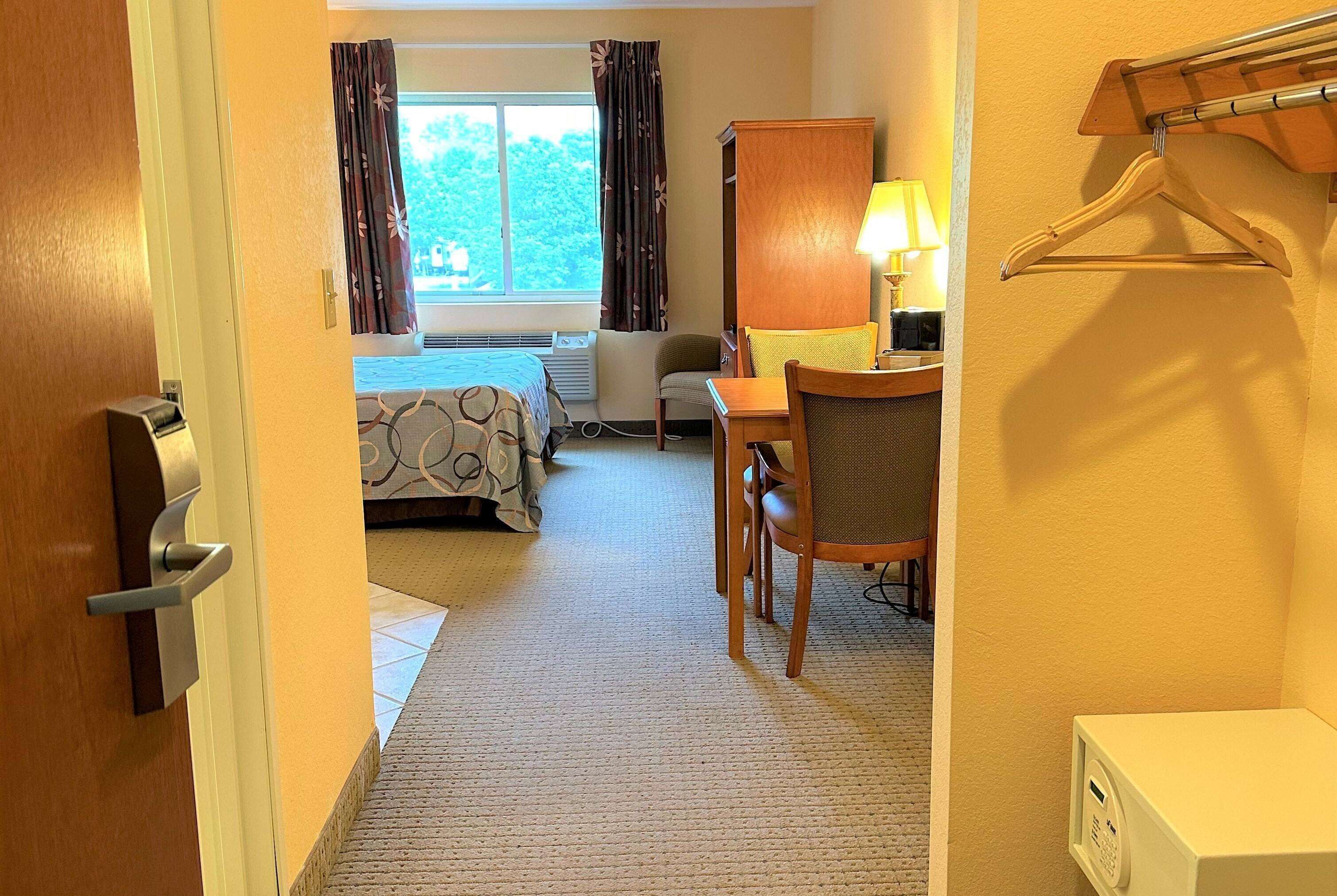 Una habitación de hotel con cama, escritorio, silla, lámpara y perchero.