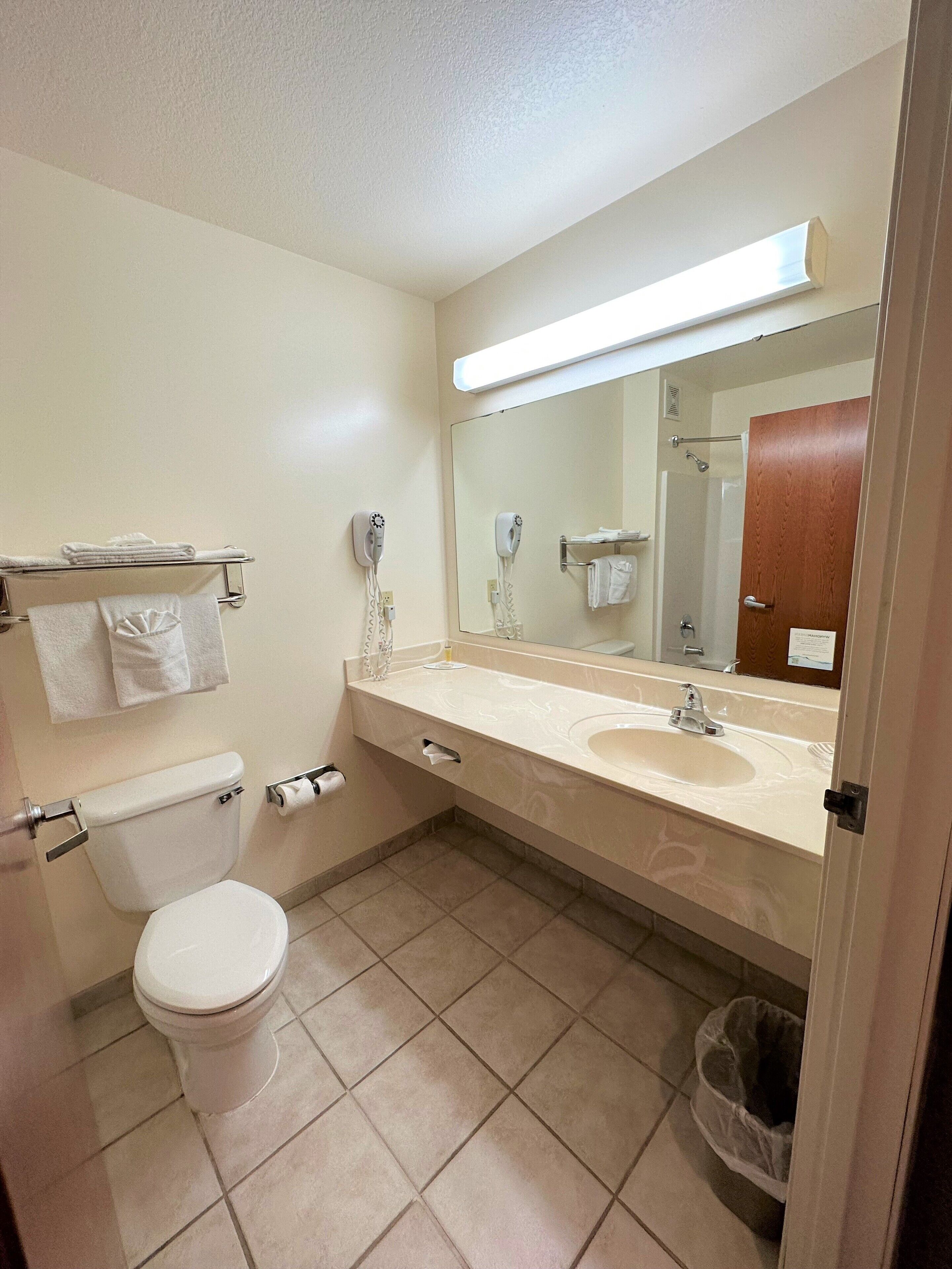 A bathroom with a toilet, sink, and mirror. There are towels on a rack and a trash can.