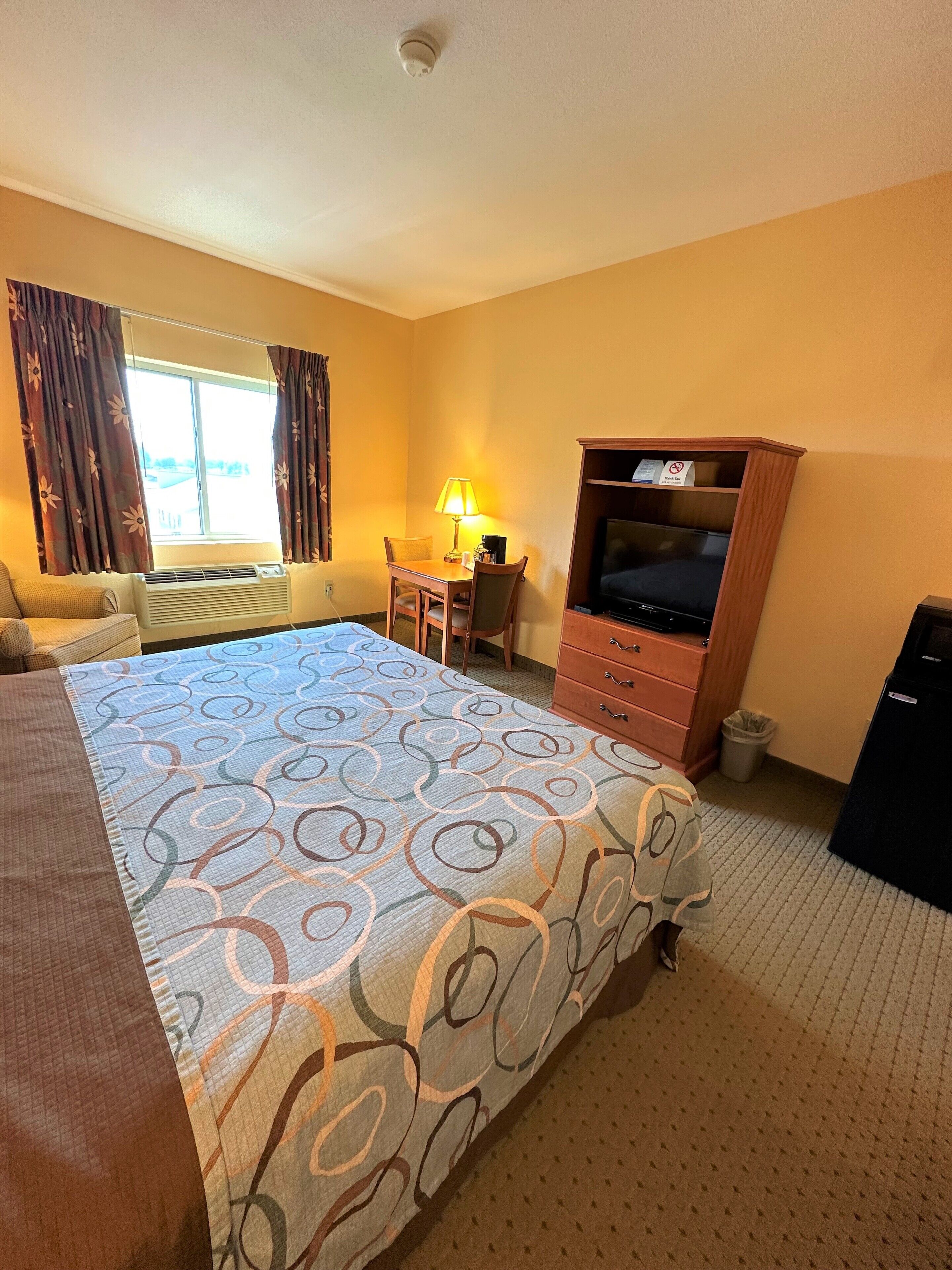 A hotel room with a large bed, a desk with a lamp, a television, and a window with curtains.