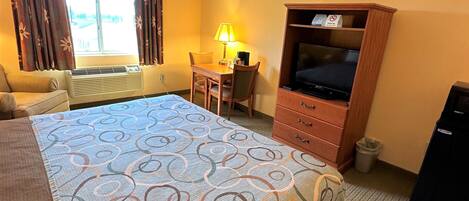 A hotel room with a large bed, a desk with a lamp, a television, and a window with curtains.