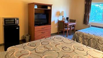 Habitación de hotel con cama, escritorio con silla, televisión, microondas y ventana con cortinas.