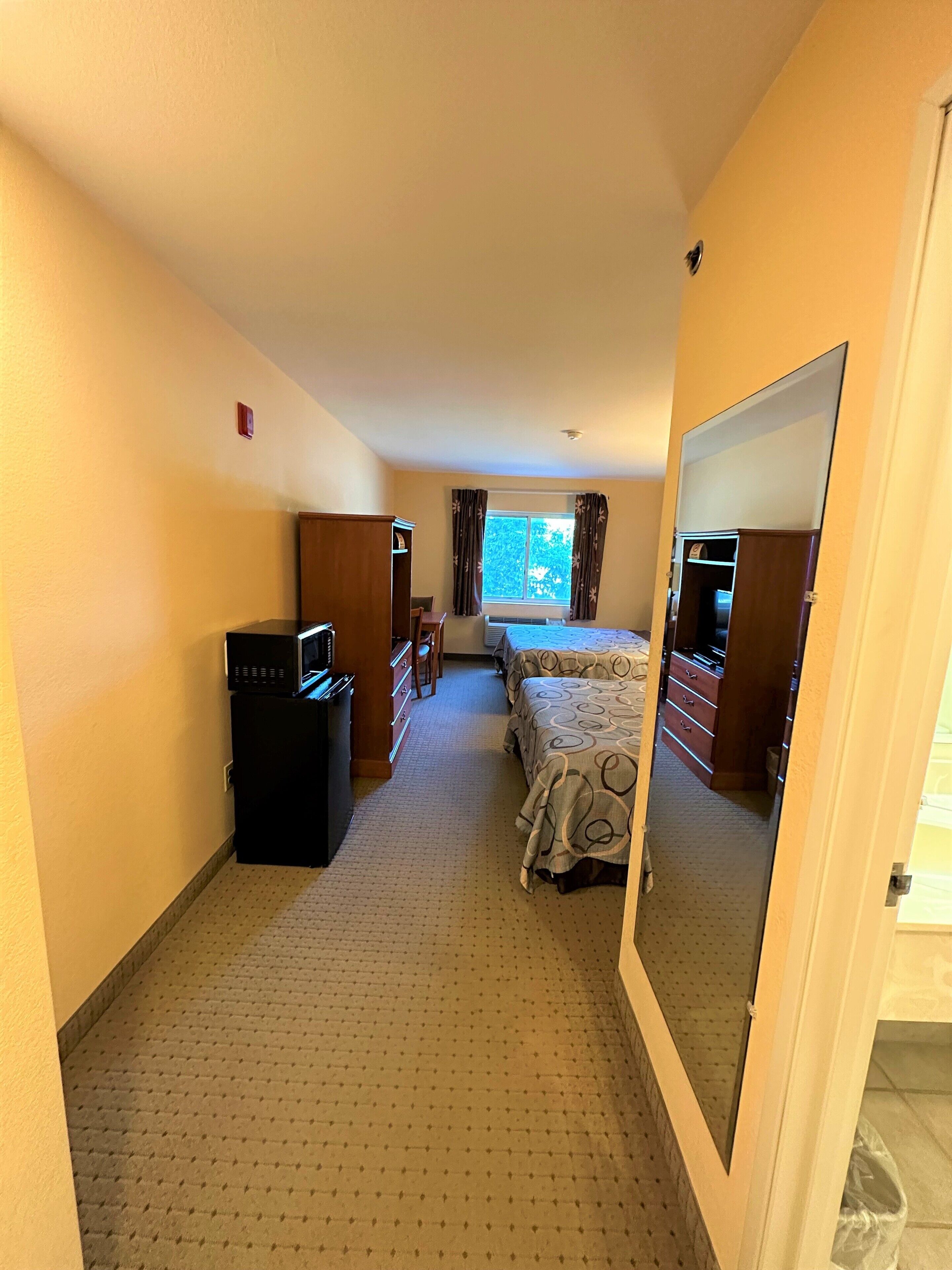 A hotel room with a bed, a desk, a dresser, and a microwave.