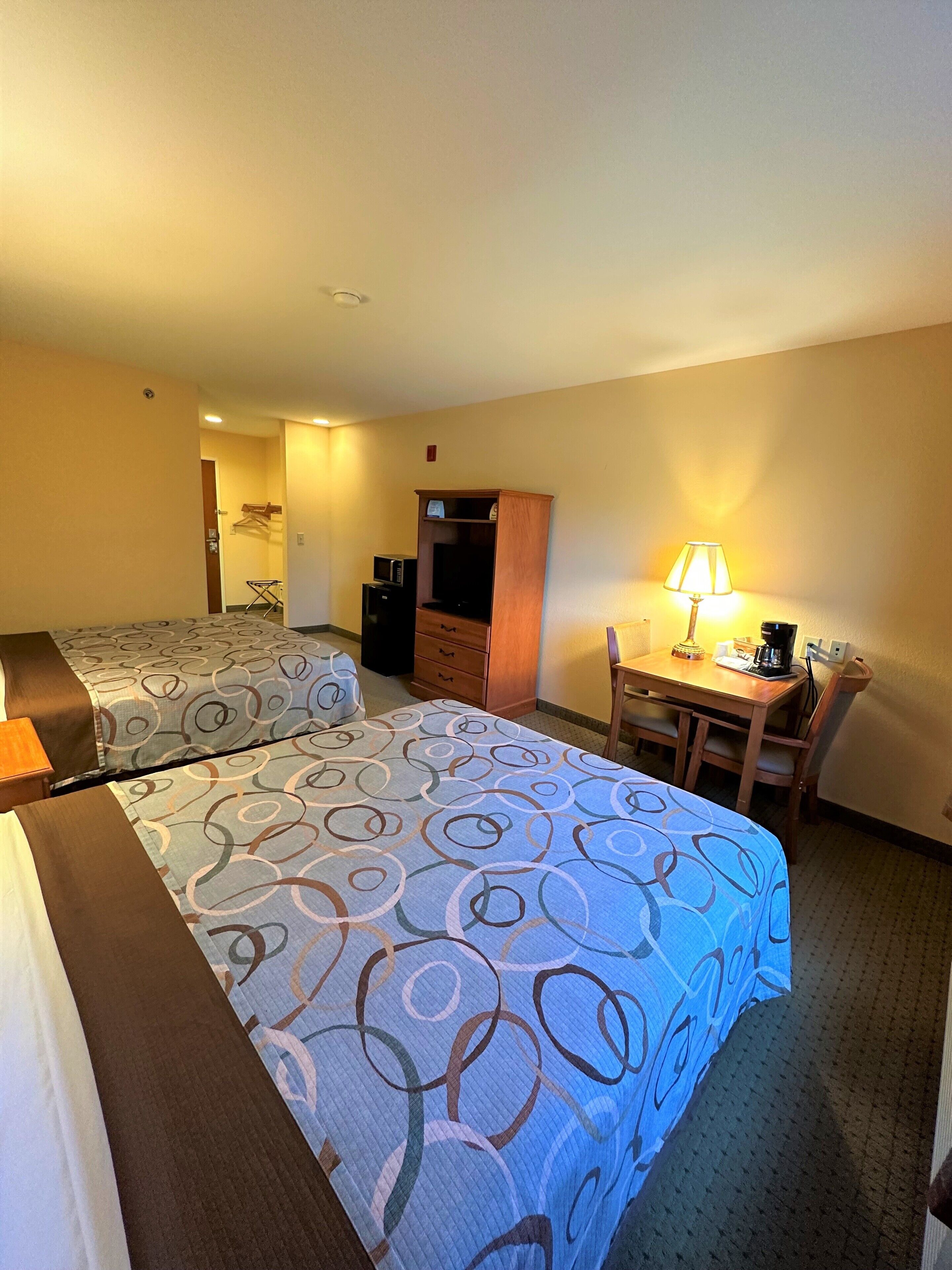 A hotel room with two beds, a desk with a lamp, a microwave, and a small cabinet.