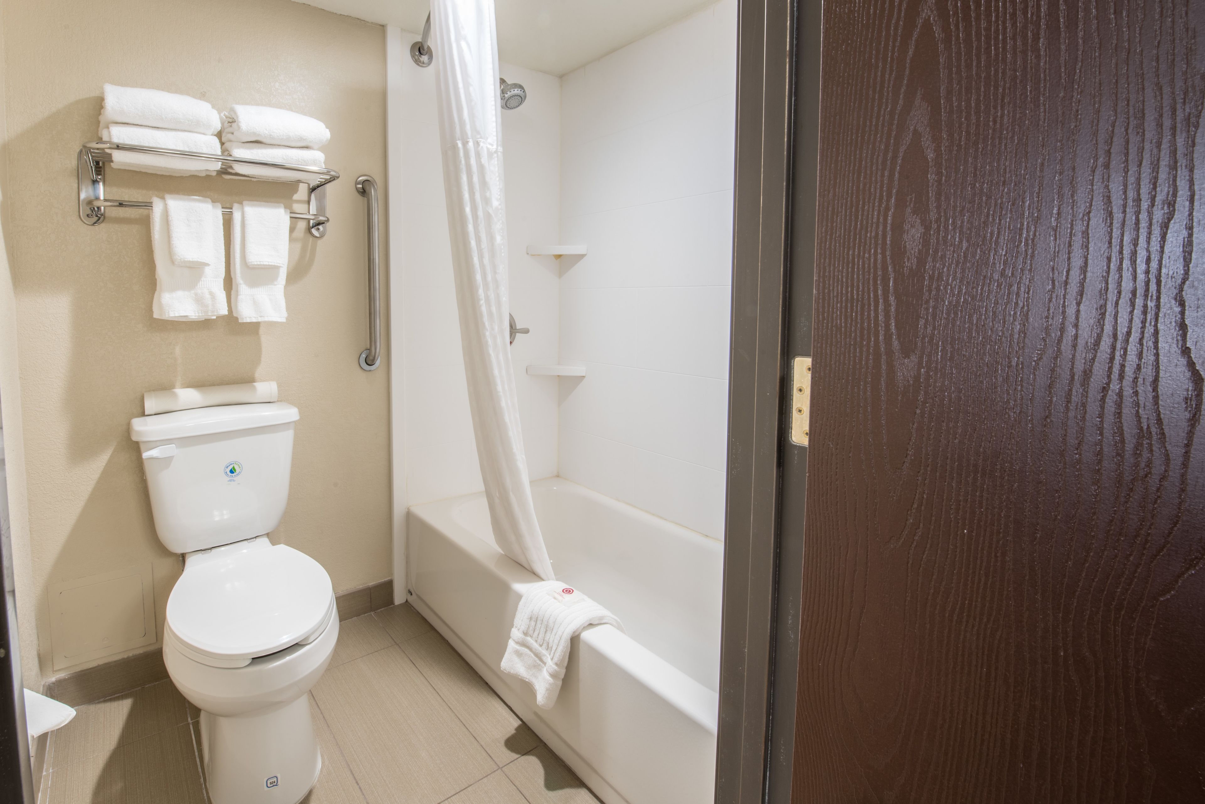 A bathroom with a toilet, a shower with a curtain, and a towel rack with multiple towels.