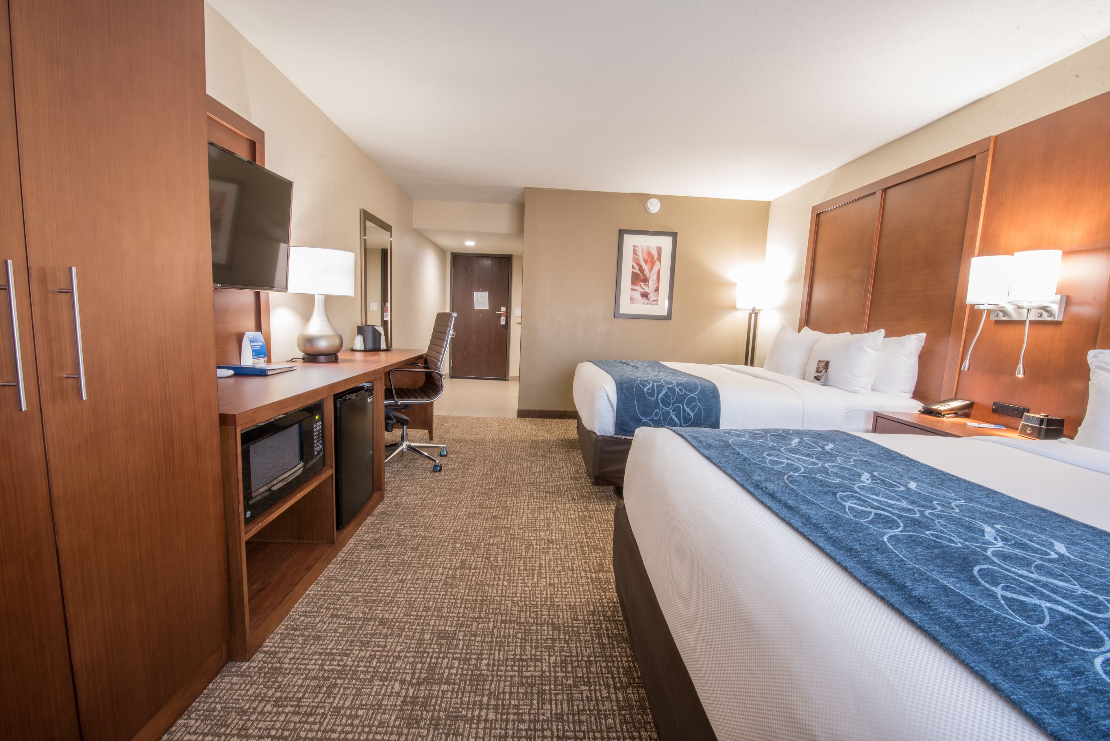 A hotel room with a desk, television, two beds, and a bathroom.