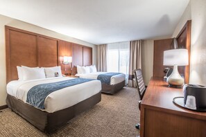 A hotel room with two beds, a desk, a lamp, and a window with curtains.