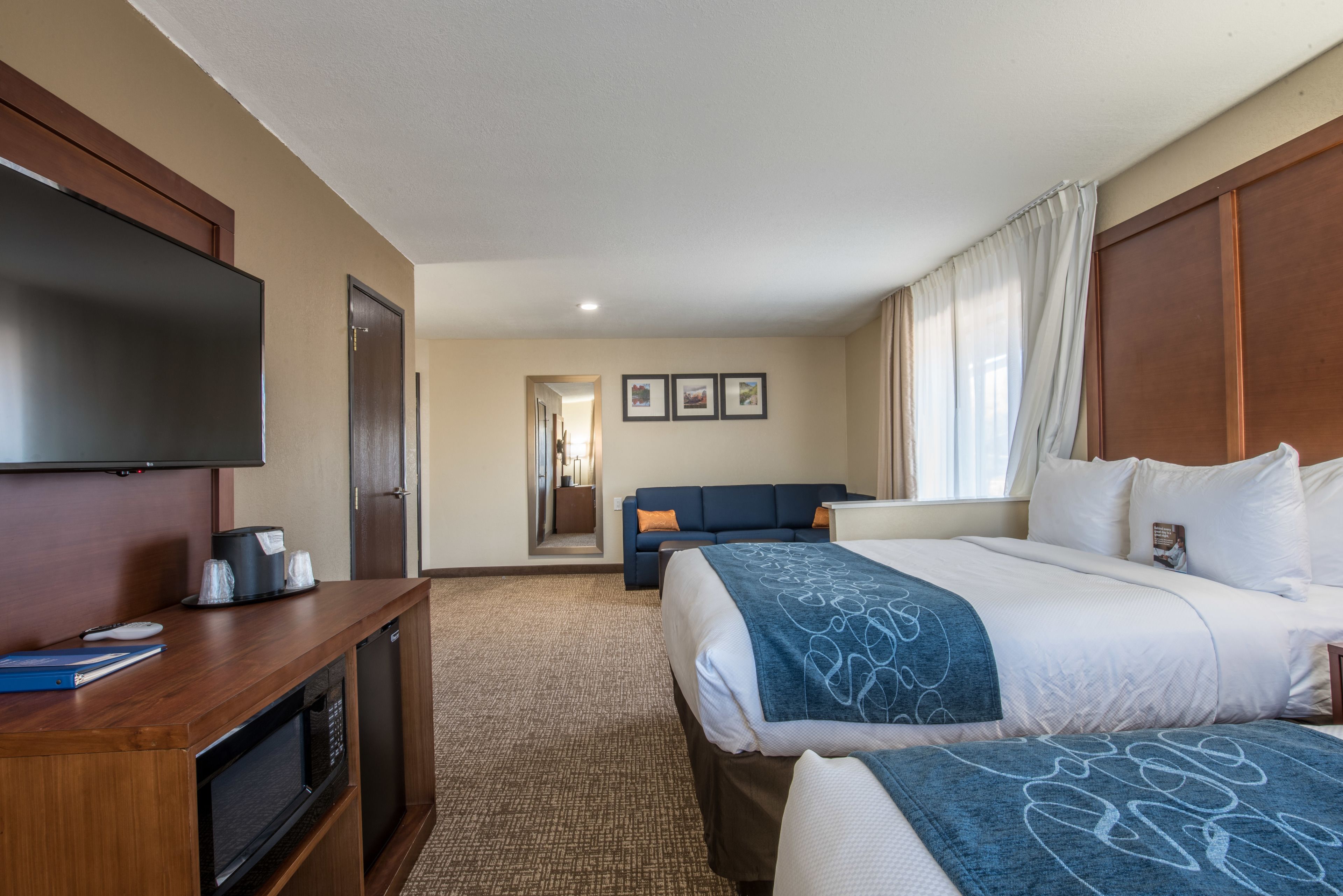 A hotel room with a large bed, a sofa, a television, a desk with a microwave, and a view of the hallway.