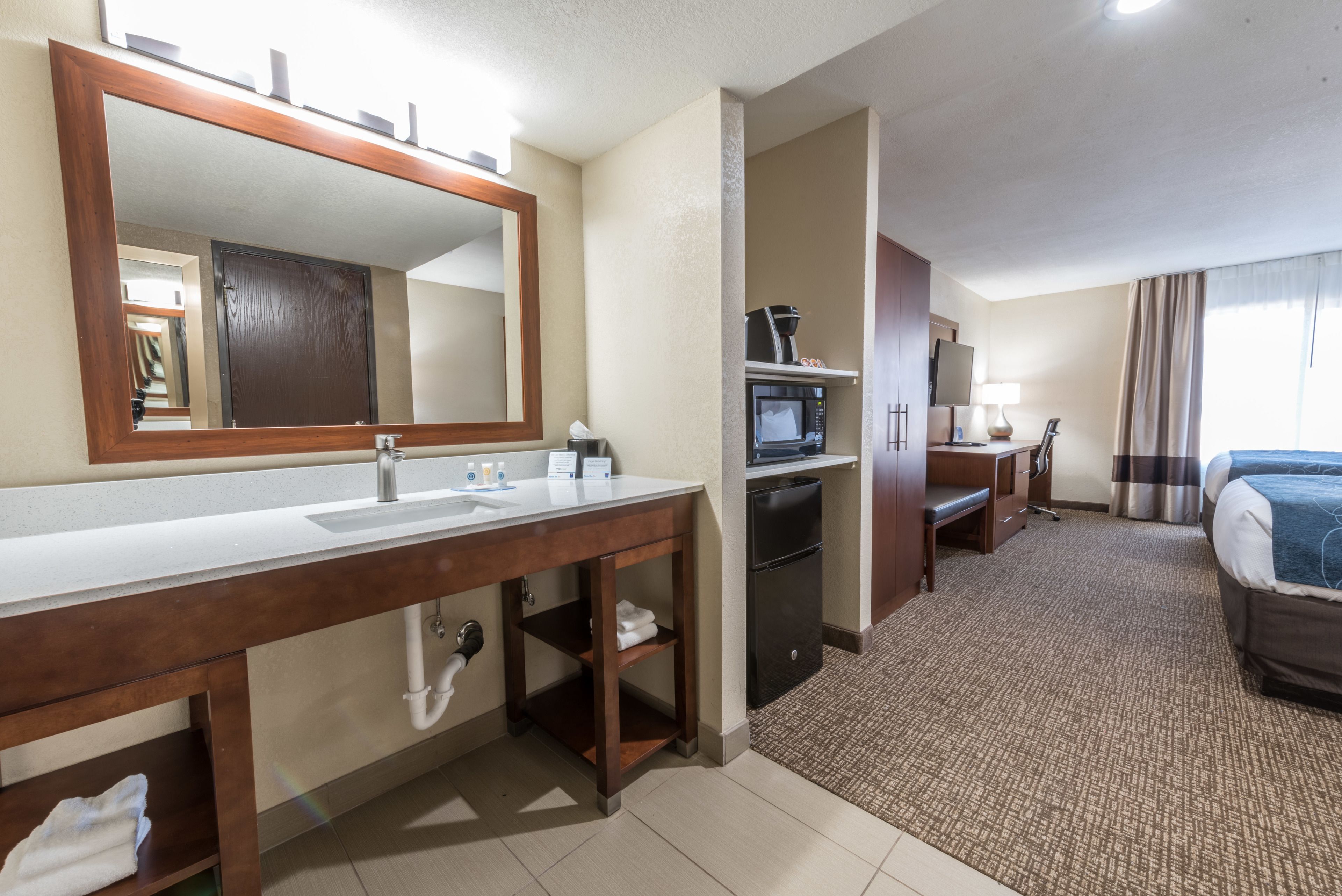 Une salle de bain d’hôtel avec un grand miroir, deux lavabos, un four à micro-ondes et un petit réfrigérateur.