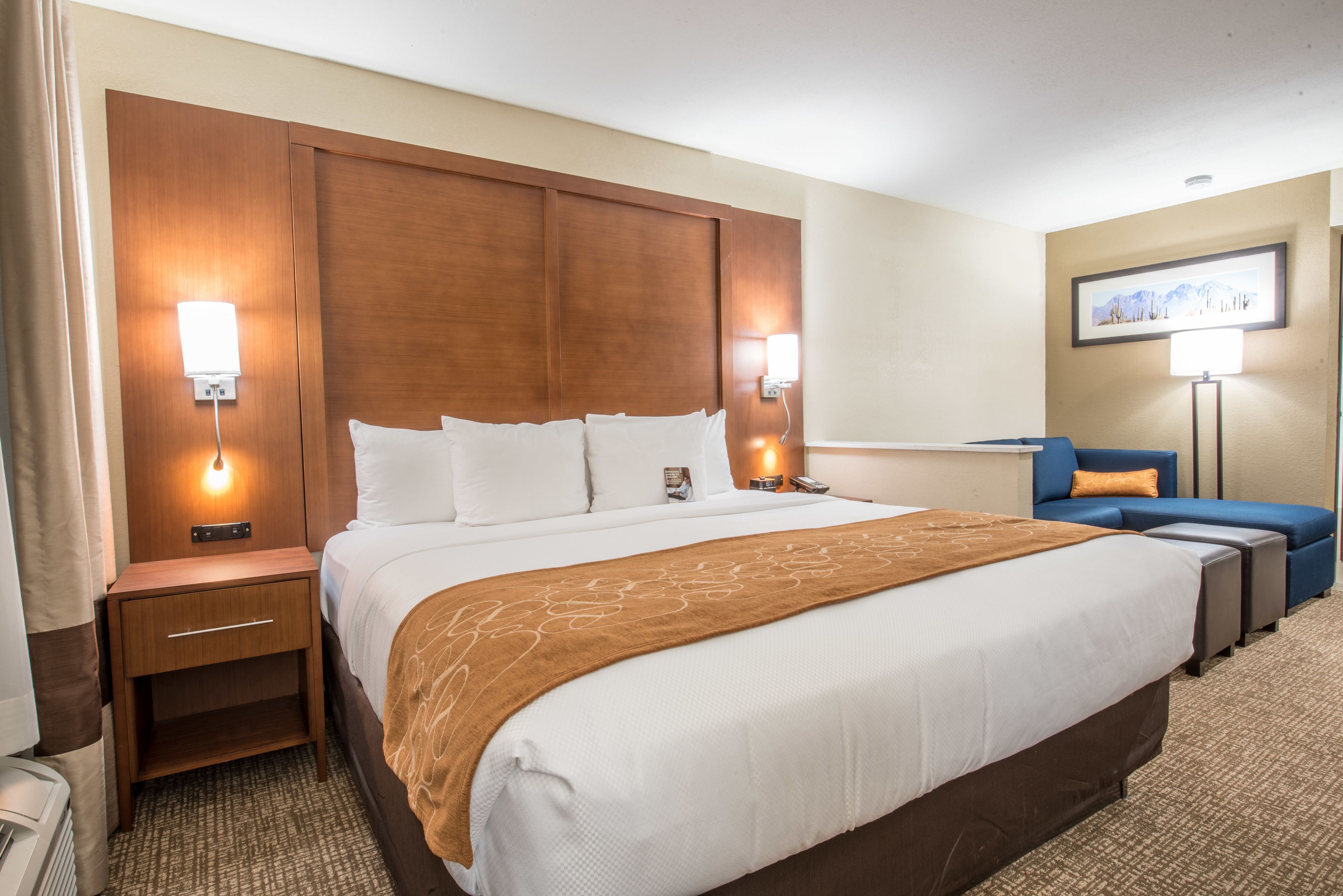 Una habitación de hotel con una cama grande, mesitas de noche, un escritorio, una silla y una lámpara.