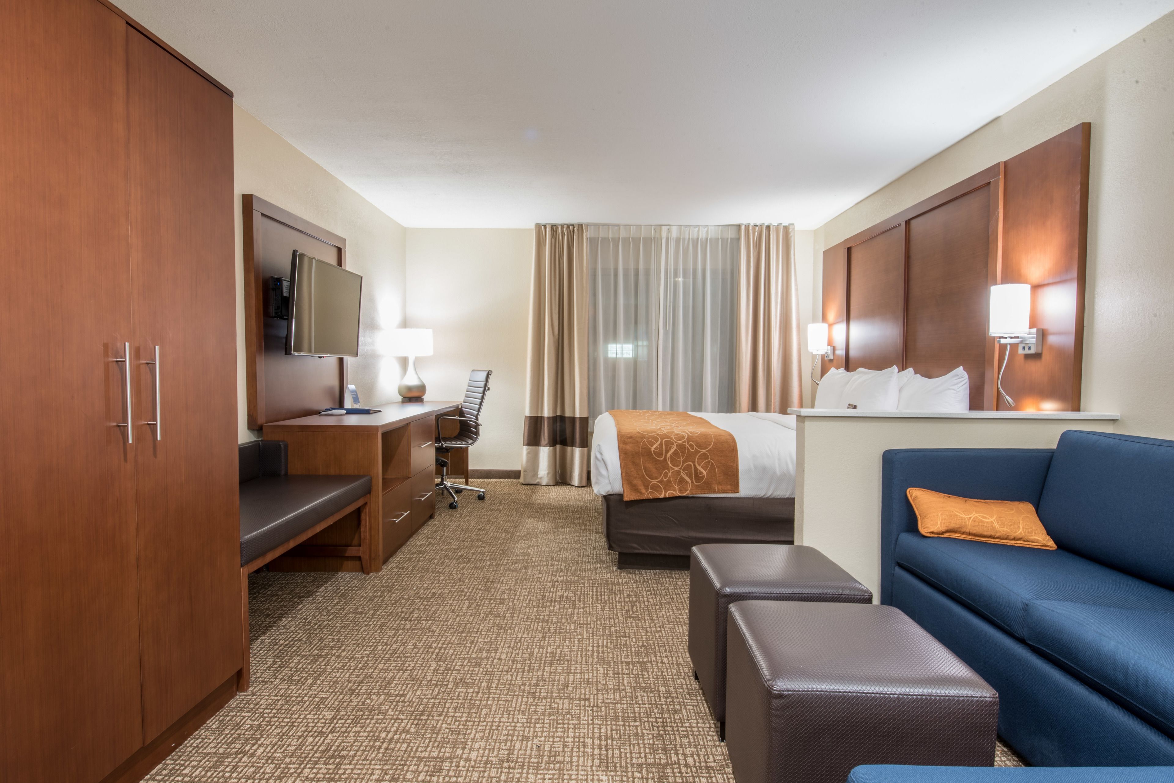 A hotel room with a bed, a desk with a chair, a sofa, a television, and a wardrobe.