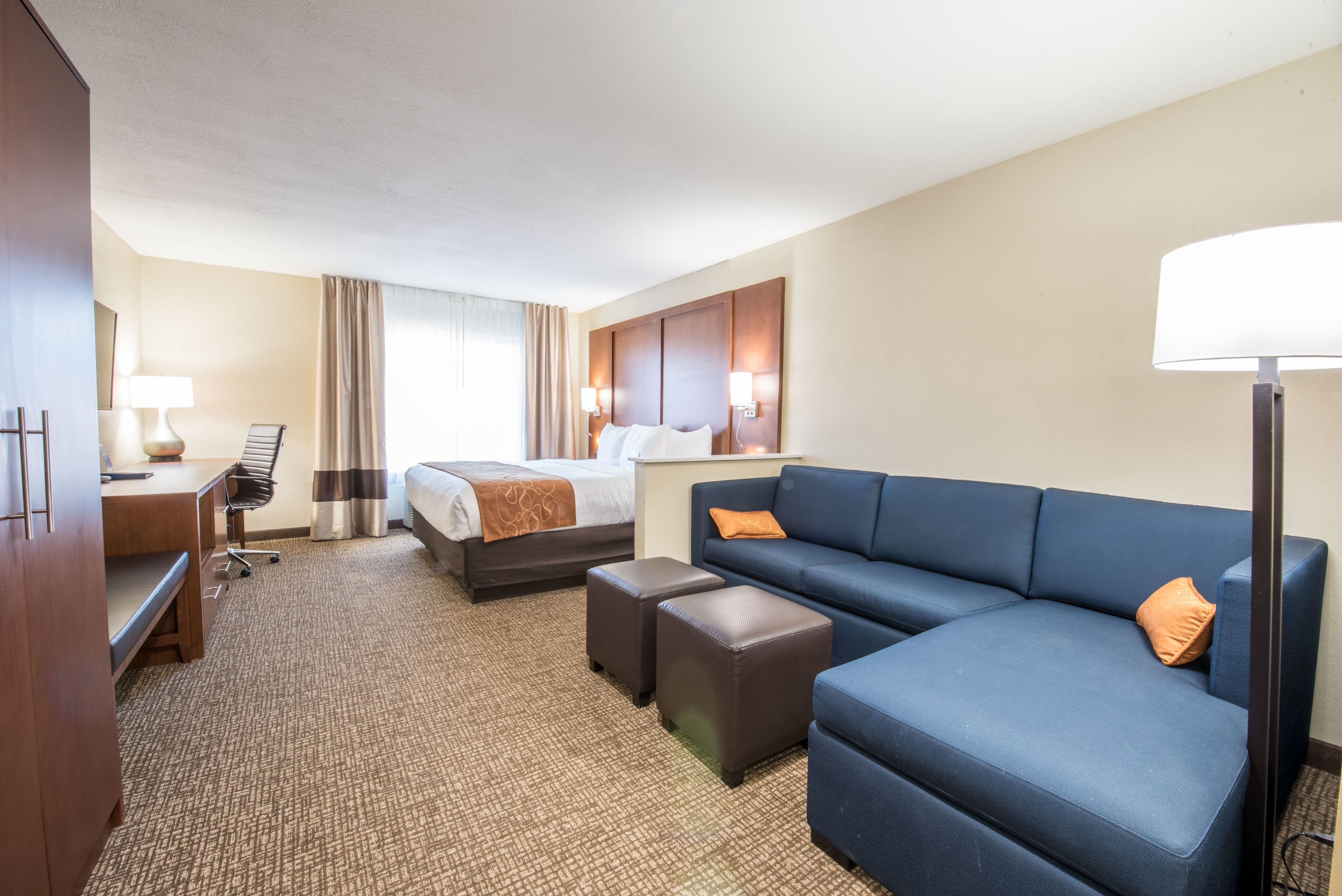 A hotel room with a bed, a sofa, a desk, and a lamp.
