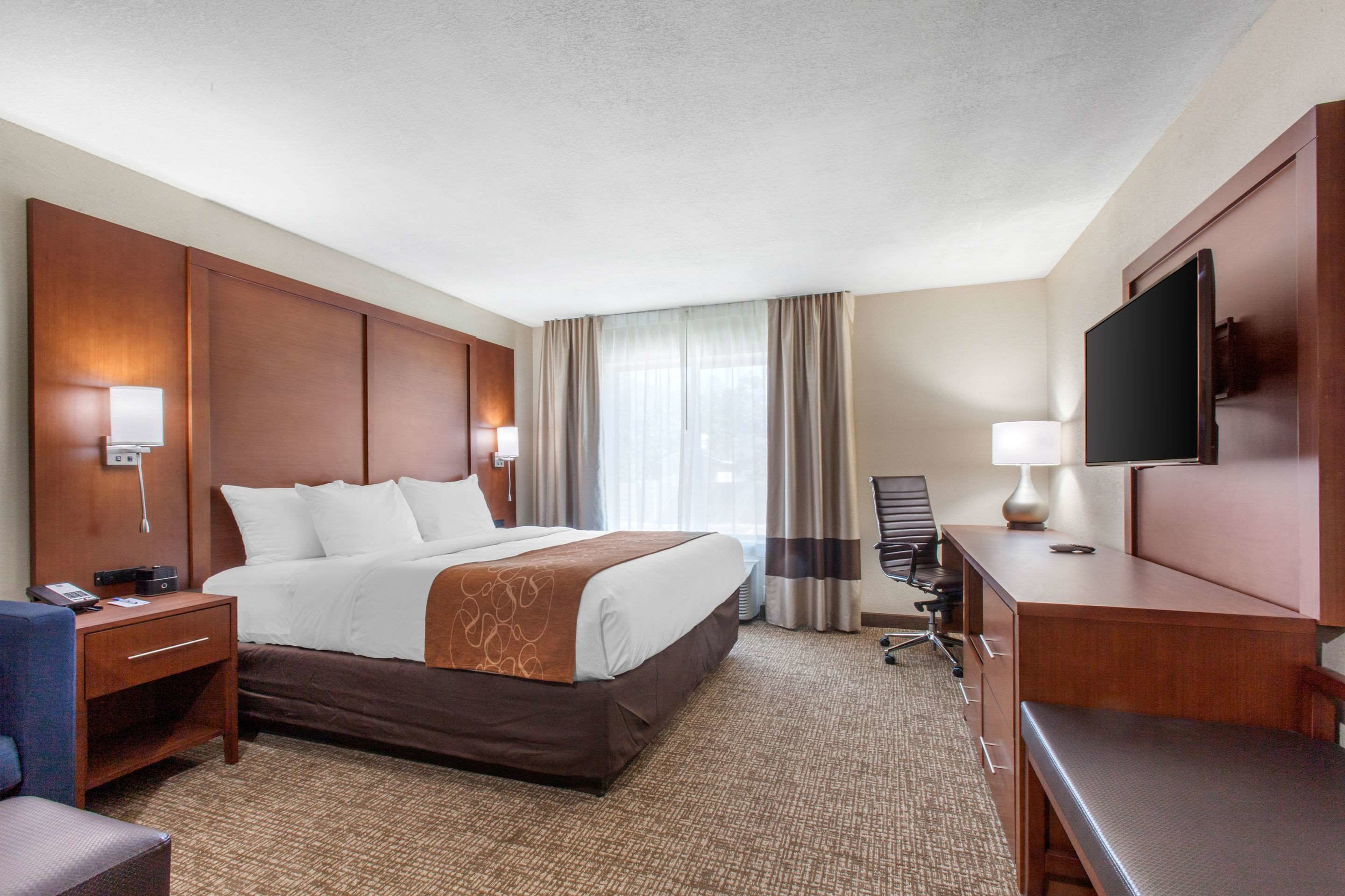 Habitación de hotel con una cama grande, un escritorio, una silla, un televisor y una ventana con cortinas.