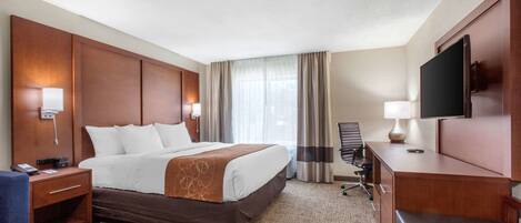 Habitación de hotel con una cama grande, un escritorio, una silla, un televisor y una ventana con cortinas.